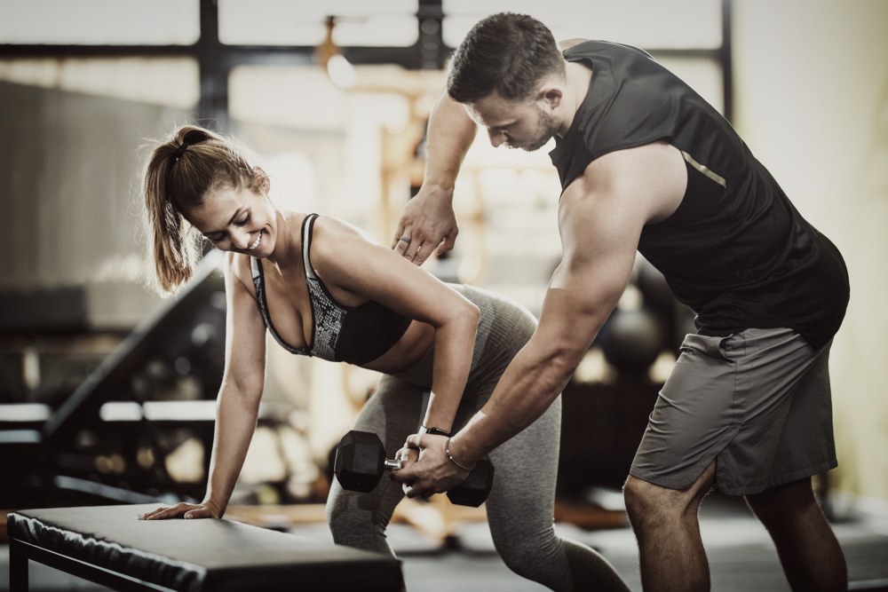 A coach guiding a beginner through a dumbbell row