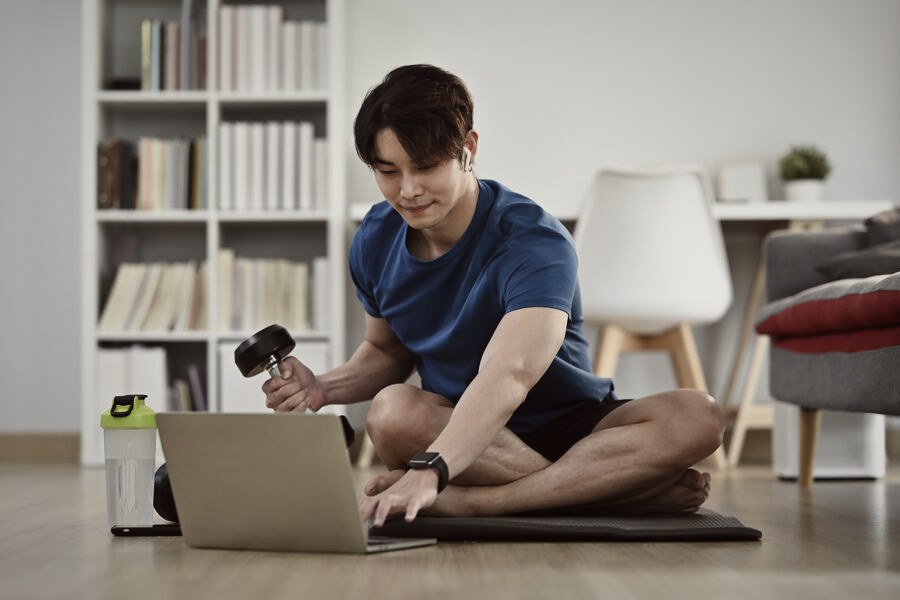 A person training with dumbbells in front of a laptop